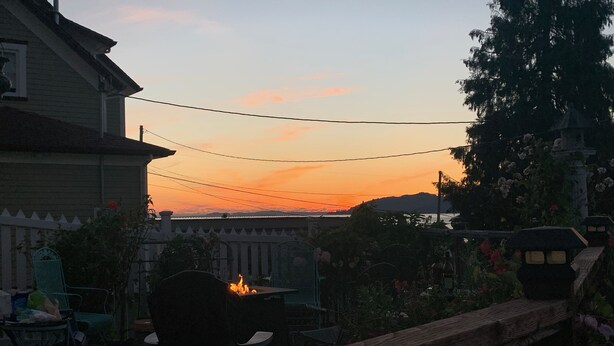 Una valla de madera, una mesa, sillas y un hogar para fuego en un patio con vistas a la puesta de sol.