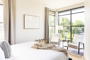 Una habitación de hotel con una cama grande, un cuadro con un mapa, una ventana con cortinas y un área de descanso con sillas y una mesa.