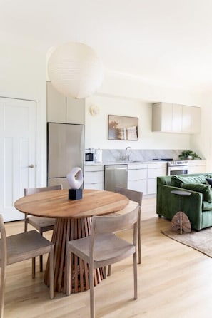 Una cocina moderna con armarios blancos, un refrigerador de acero inoxidable y un comedor con una mesa y sillas de madera.