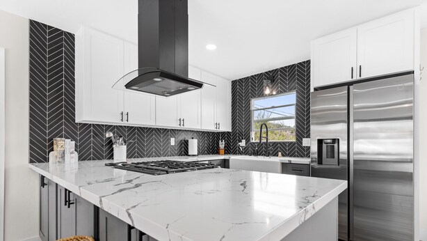 A modern kitchen with a large island, stainless steel appliances, and a black and white herringbone backsplash.