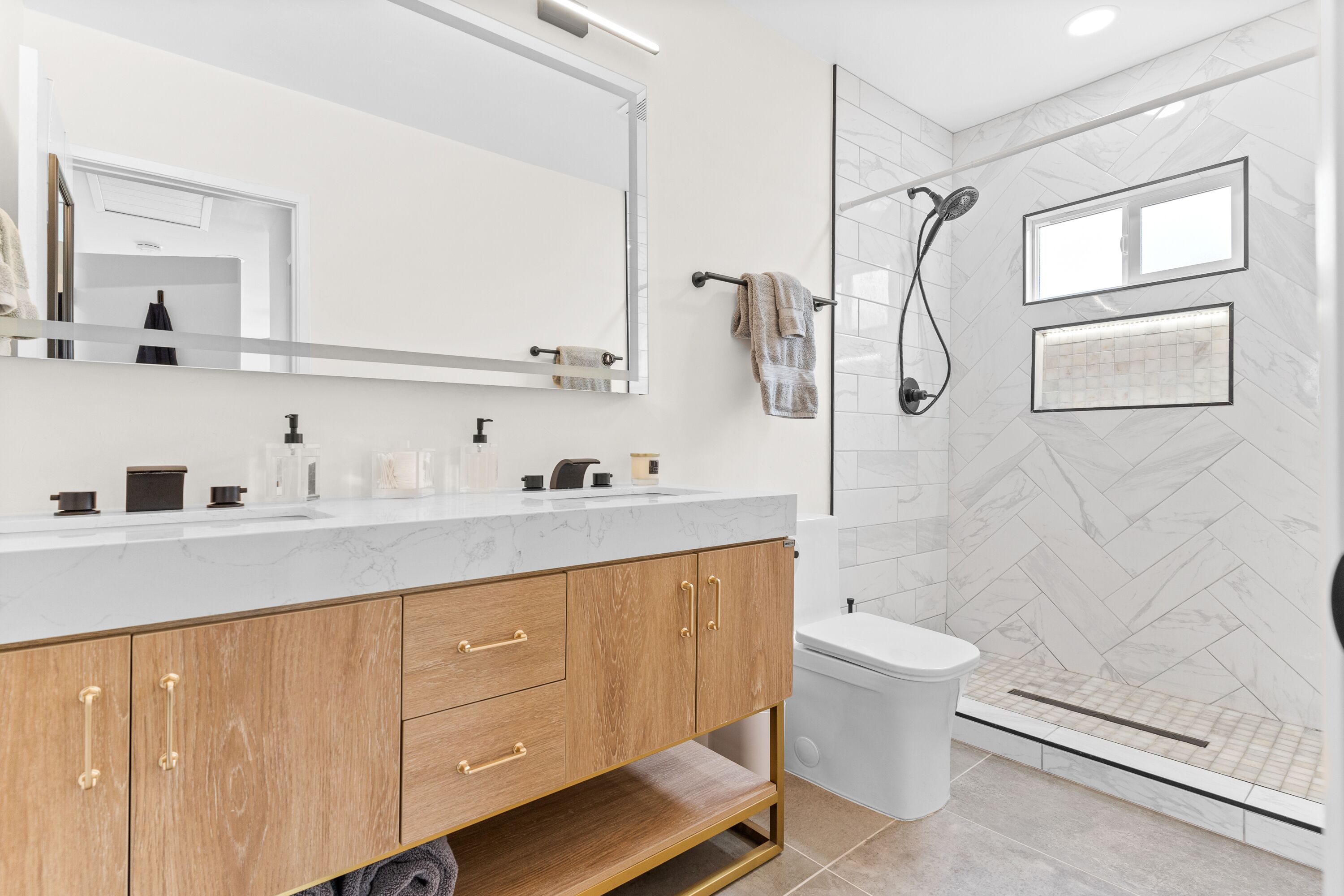 Un baño moderno con tocador de mármol, un espejo grande, ducha con puerta de vidrio y un inodoro.