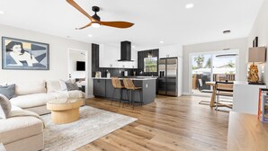 A modern kitchen with a central island, a dining area with a table and chairs, and a living room with a sofa and a coffee table.