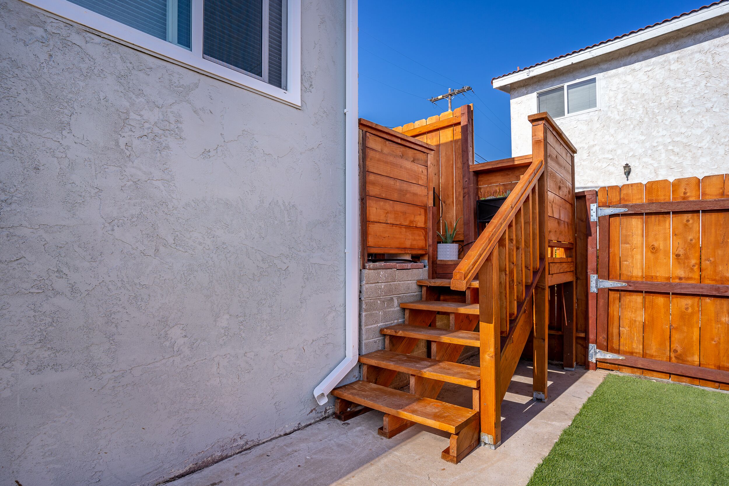 A wooden staircase leading to a door, a white wall, and a wooden fence.