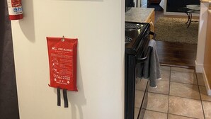 A kitchen with a stove, a fire extinguisher, and a red fire blanket on the wall. - Your home away from home (Abbotsford)