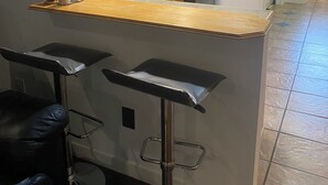 A kitchen with wooden cabinets, a black refrigerator, a hanging clock, and a bar area with stools. - Your home away from home (Abbotsford)