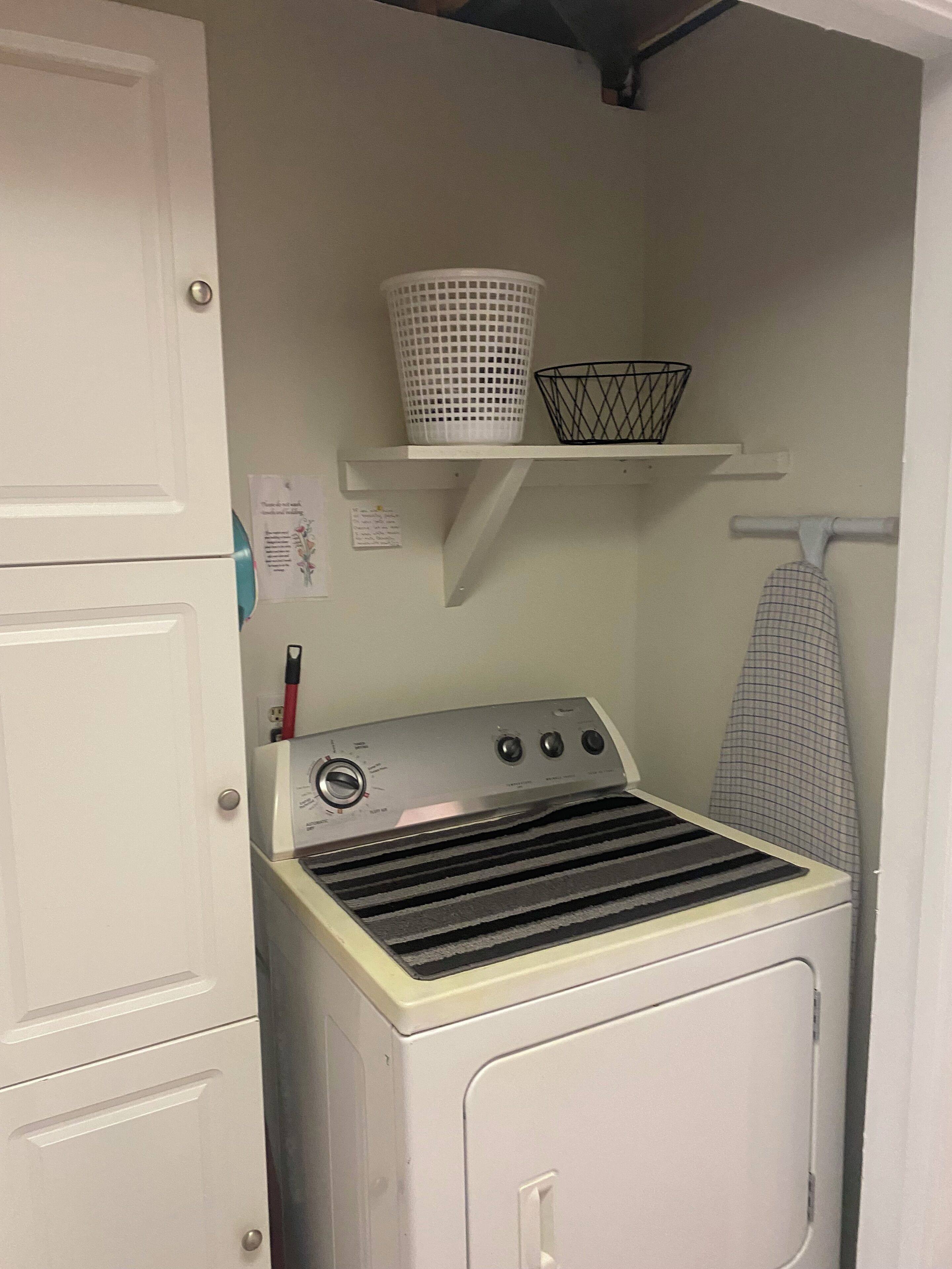 A laundry room with a washer and dryer, a shelf with baskets, and a hanging iron.