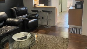 A modern living room with a leather sofa, a glass coffee table, and a kitchen area in the background. - Your home away from home (Abbotsford)