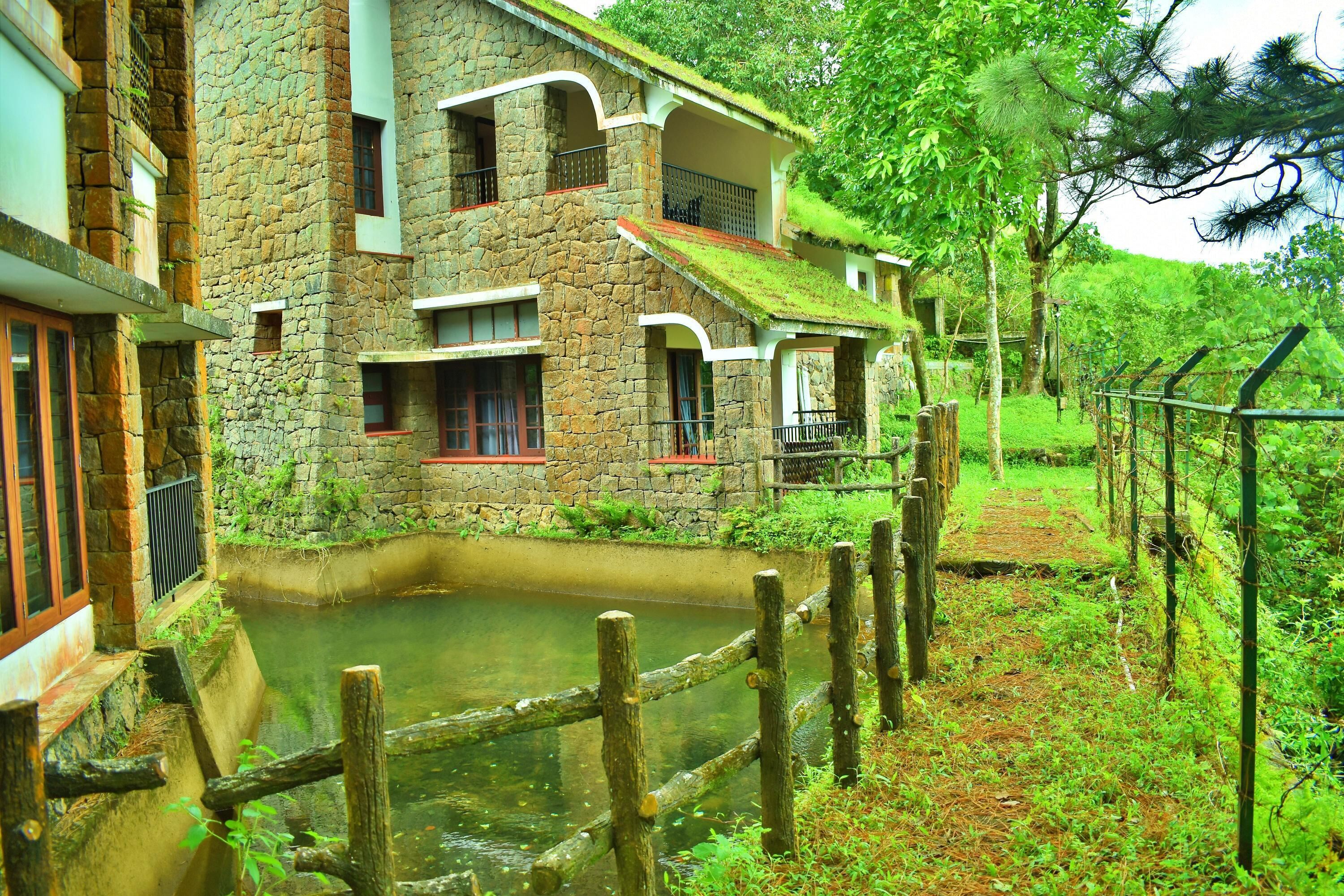 A stone building with a pond in front, surrounded by greenery.