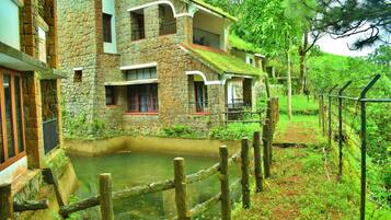 A stone building with a pond in front, surrounded by greenery.