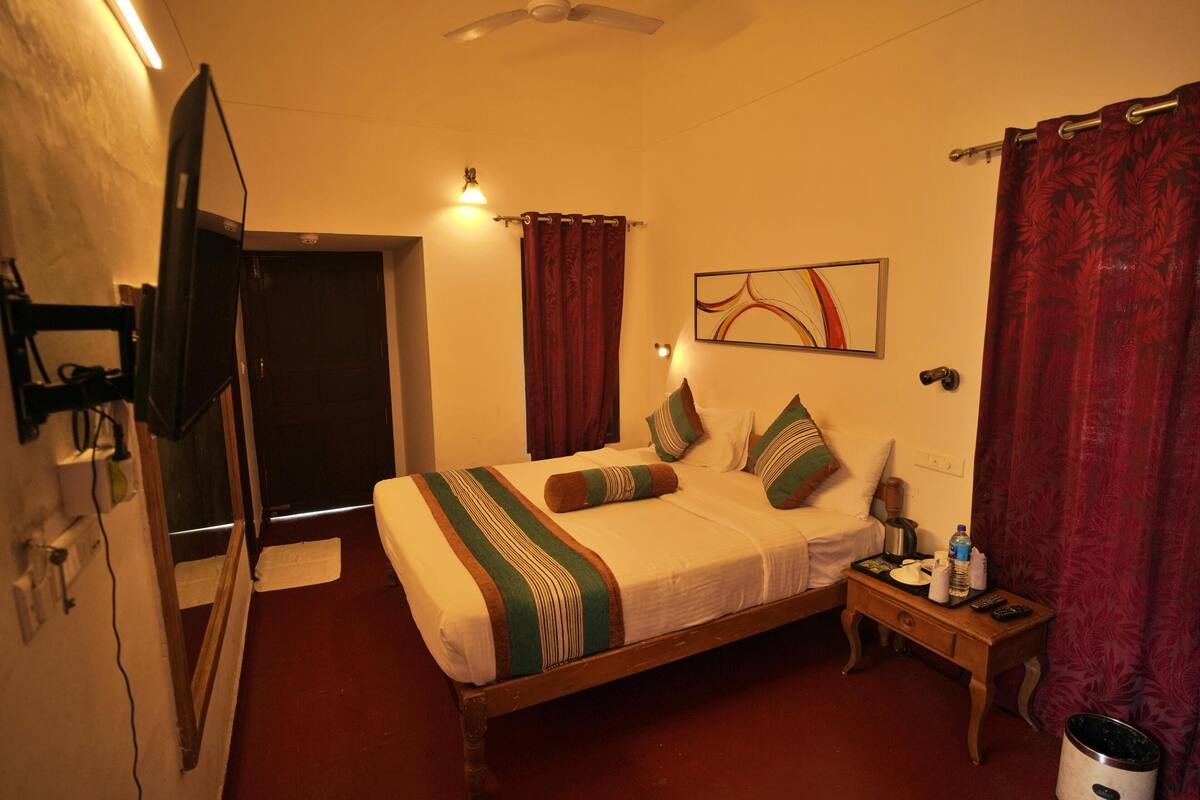 Una habitación de hotel con cama, mesita de noche, televisor y puerta.