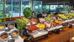 A buffet with various food items and a view of greenery outside.