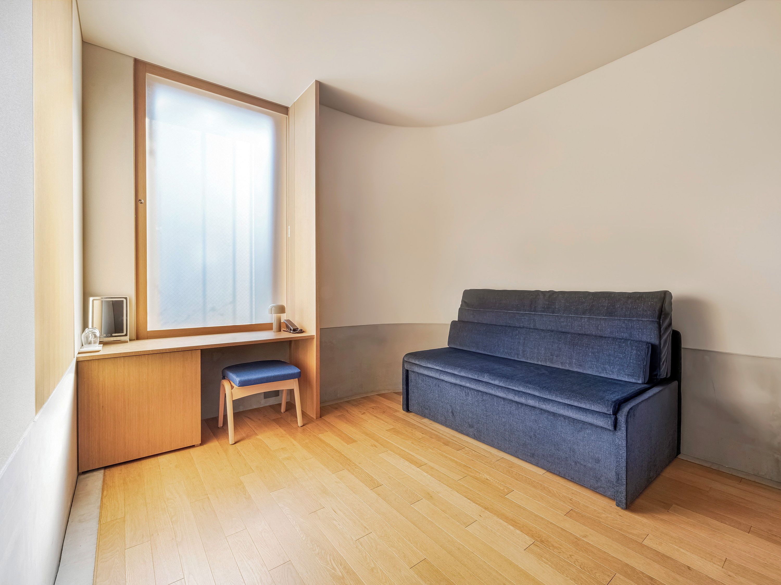 Una habitación con un escritorio de madera, un banco azul y una ventana con persianas.