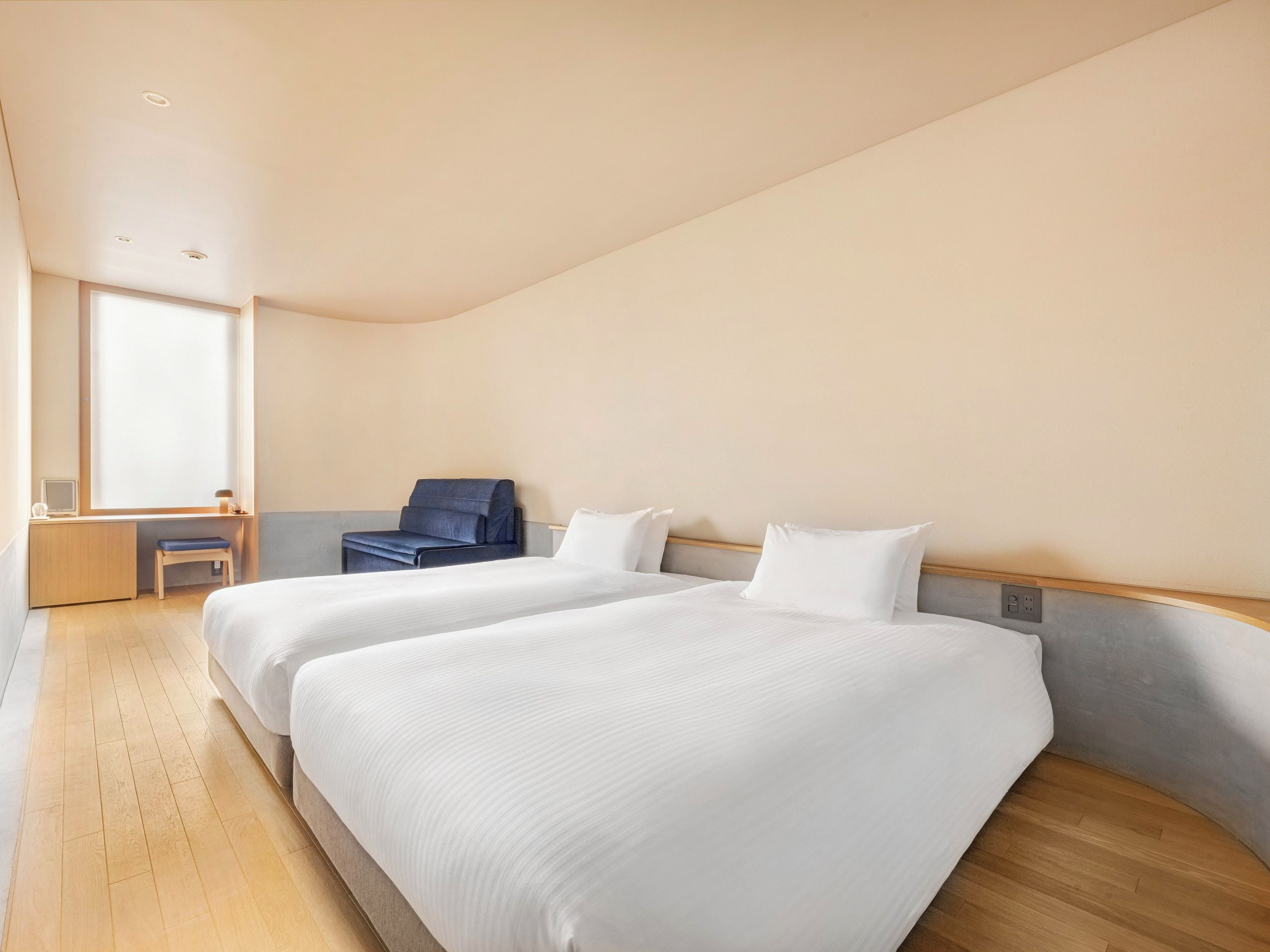 A hotel room with two beds, a desk, a chair, and a large window.