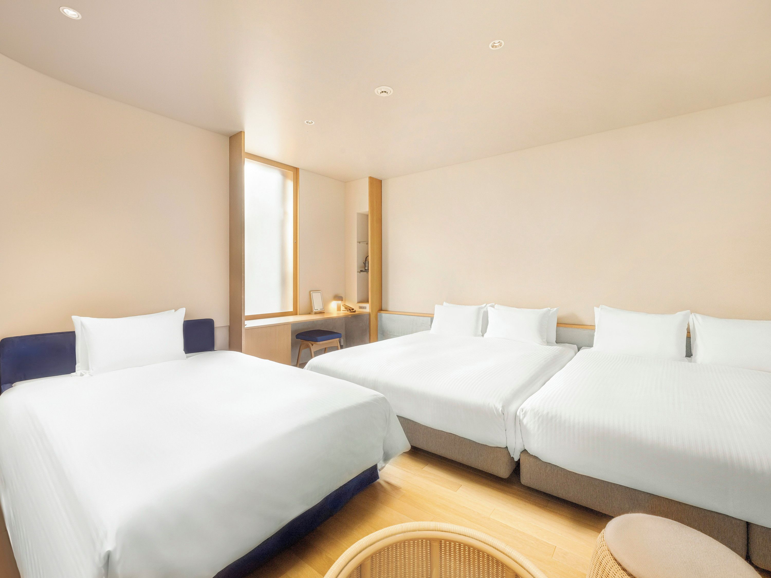A hotel room with two beds, a desk, a chair, and a large window.