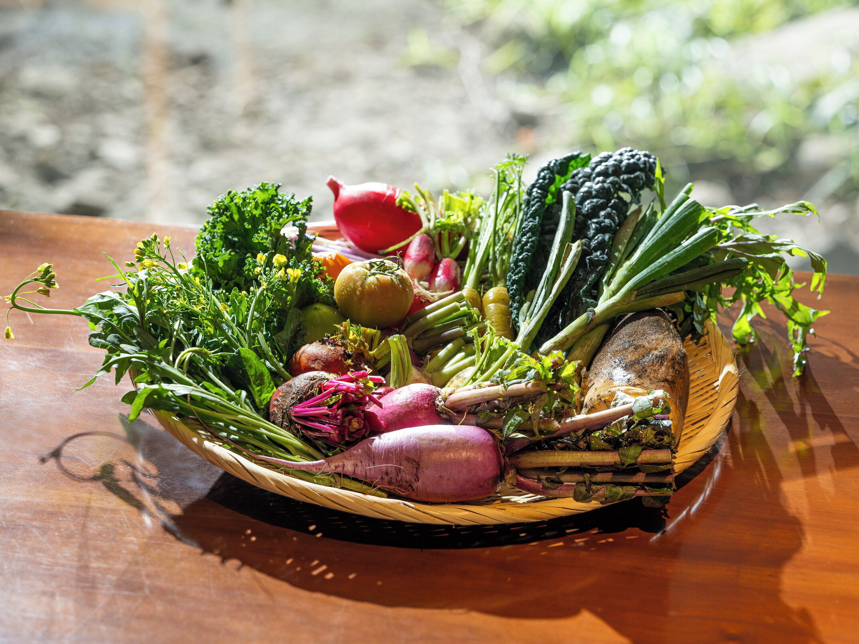 A basket of fresh vegetables on a wooden table.