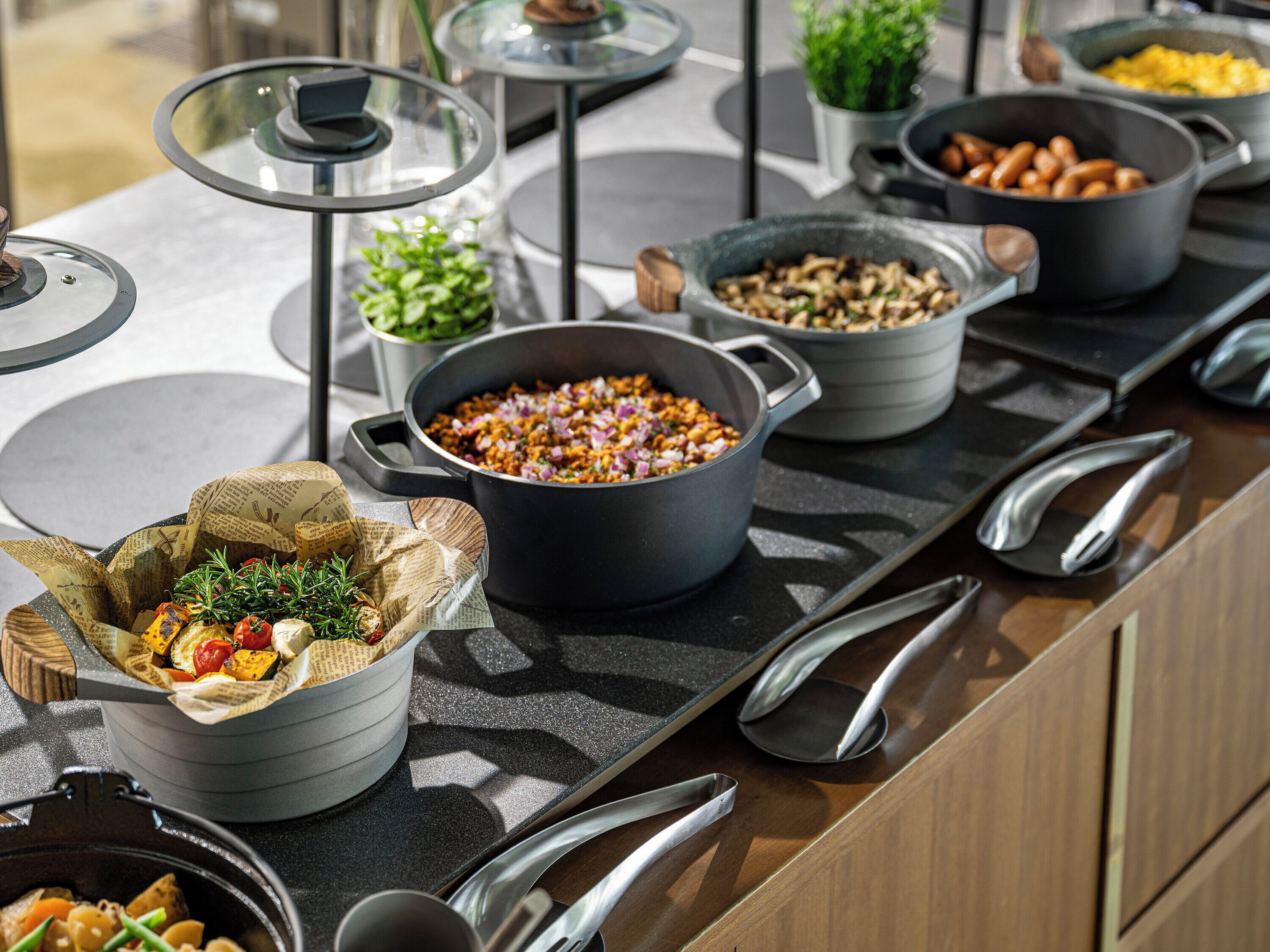 A buffet setup with various dishes in pots and bowls, arranged on a countertop with utensils.