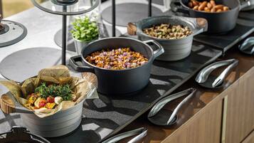 A buffet setup with various dishes in pots and bowls, arranged on a countertop with utensils.