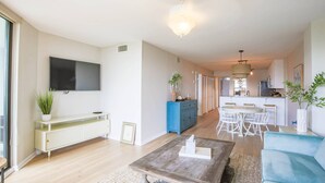 Un soggiorno moderno con televisione a schermo piatto, tavolino e divano. Sullo sfondo, una zona cucina con tavolo e sedie.