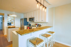 A modern kitchen with white cabinetry, a granite countertop, and a central island with bar stools.