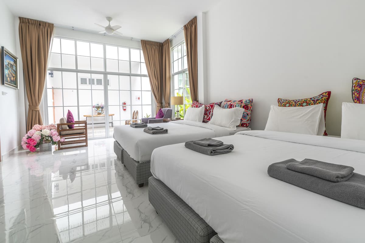 Une chambre d’hôtel avec deux lits, une grande fenêtre avec des rideaux, un ventilateur de plafond et une vue sur l’extérieur.