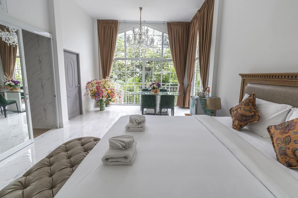 Une chambre spacieuse avec un grand lit, un bureau et une vue sur la verdure par la fenêtre.