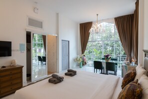 Habitació d'hotel amb un llit gran, una taula de treball amb cadires, un penjallum i vista a verdura per la finestra.