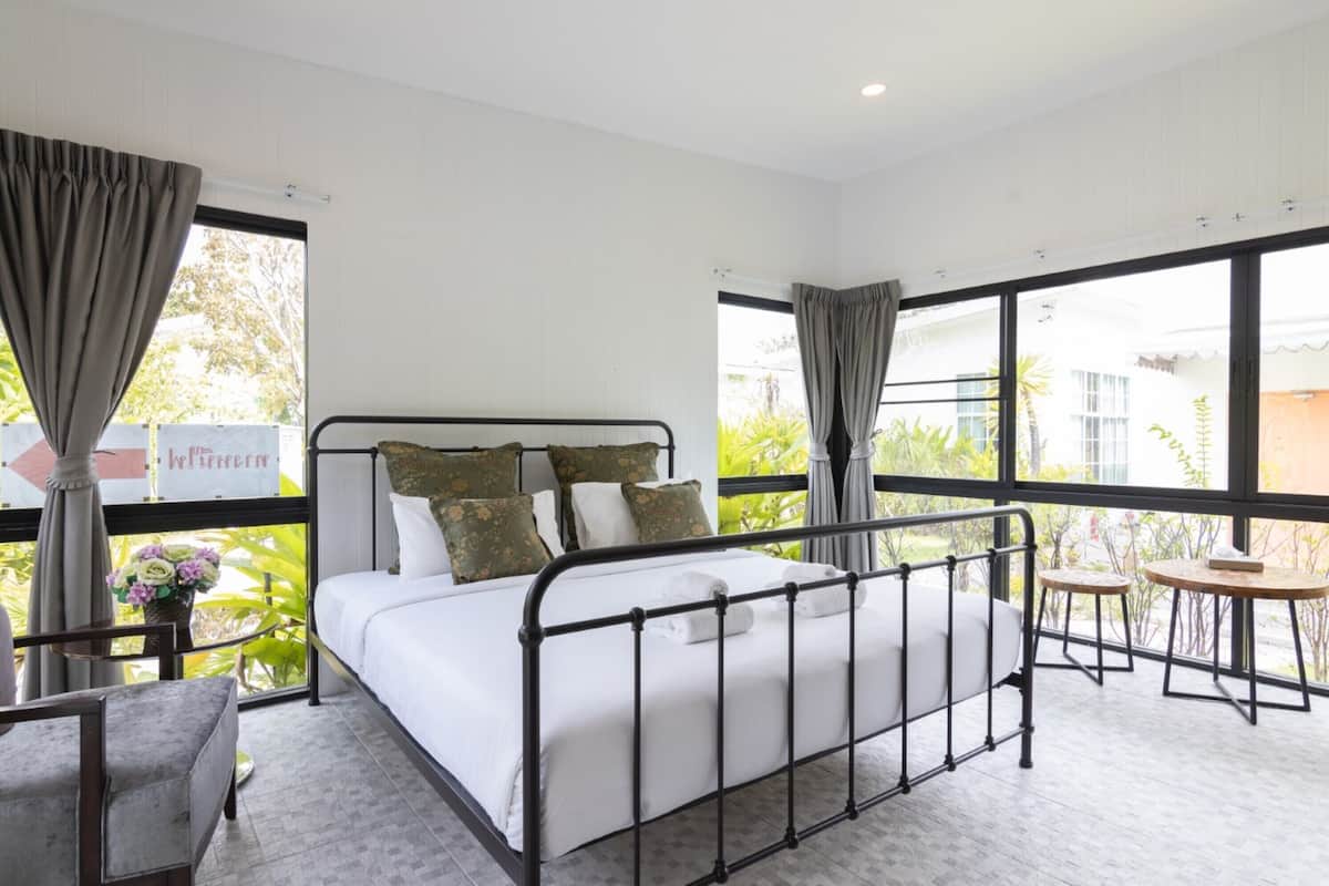 Une chambre moderne avec un lit à structure métallique, de grandes fenêtres et une vue sur la verdure environnante.