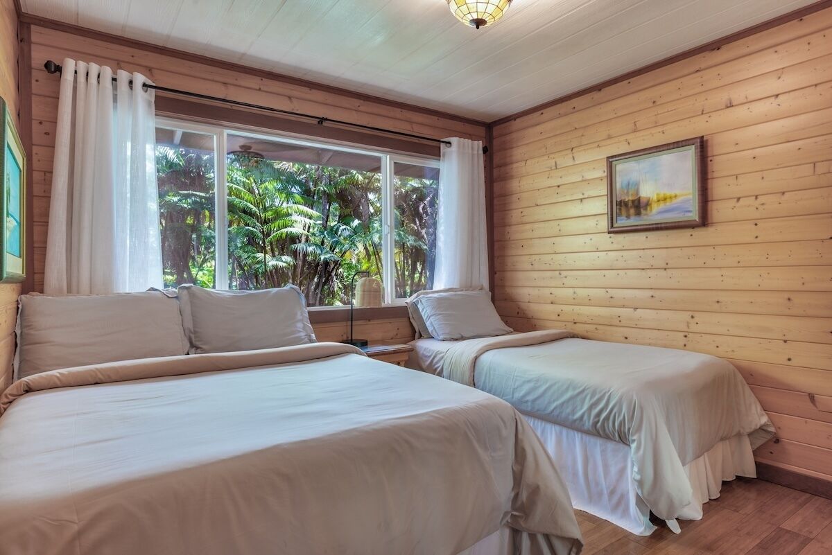 Una habitación con dos camas, una ventana con cortinas, un cuadro en la pared y paneles de madera.