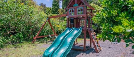 Une structure de jeu en bois dotée de deux toboggans et d’une échelle d’escalade.