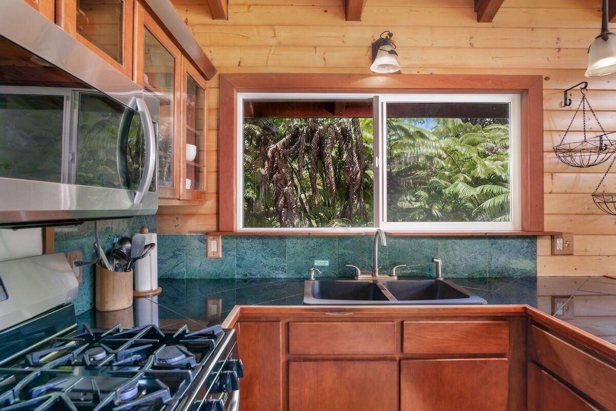 A kitchen with wooden cabinets, a stainless steel microwave, a gas stove, a window with a view of greenery, and a hanging light fixture.