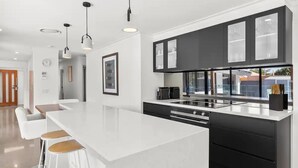 Une cuisine moderne dotée d’un grand îlot central, de meubles de couleur noire et de luminaires suspendus.