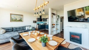 Una sala de estar moderna con una mesa de comedor de madera preparada para cuatro personas, un sofá gris y un televisor montado en la pared.