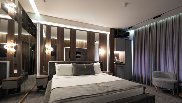 A modern hotel room with a large bed, a bedside table, a chair, a mirror, and a curtain. - Merida Hotel Baku (Baku)