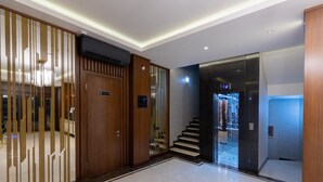 A modern hotel lobby with a polished marble floor, a wooden reception desk, and a staircase leading to another level. - Merida Hotel Baku (Baku)