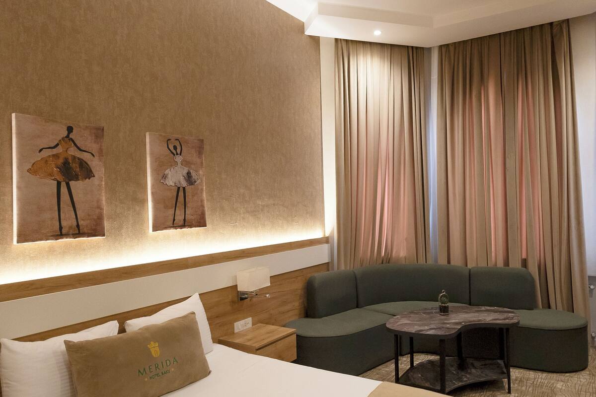 A hotel room with a large bed, a sofa, a small table, and a wall-mounted artwork.