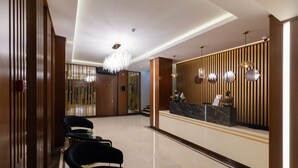 A hotel reception area with a polished marble floor, a reception desk with a wooden panel backdrop, and a chandelier. - Merida Hotel Baku (Baku)
