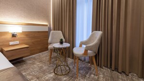 A hotel room with a bed, two armchairs, a small round table, a nightstand, a lamp, and a window with curtains. - Merida Hotel Baku (Baku)