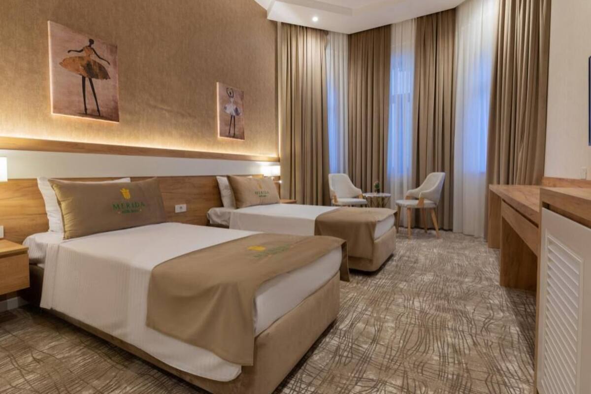A hotel room with two beds, a desk, a chair, and a large window with curtains.