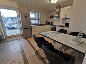 Une cuisine moderne avec une table à manger, des chaises, un réfrigérateur et une fenêtre.