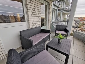 Un balcon agrémenté de meubles en osier, d’une plante en pot et offrant une vue sur la ville.