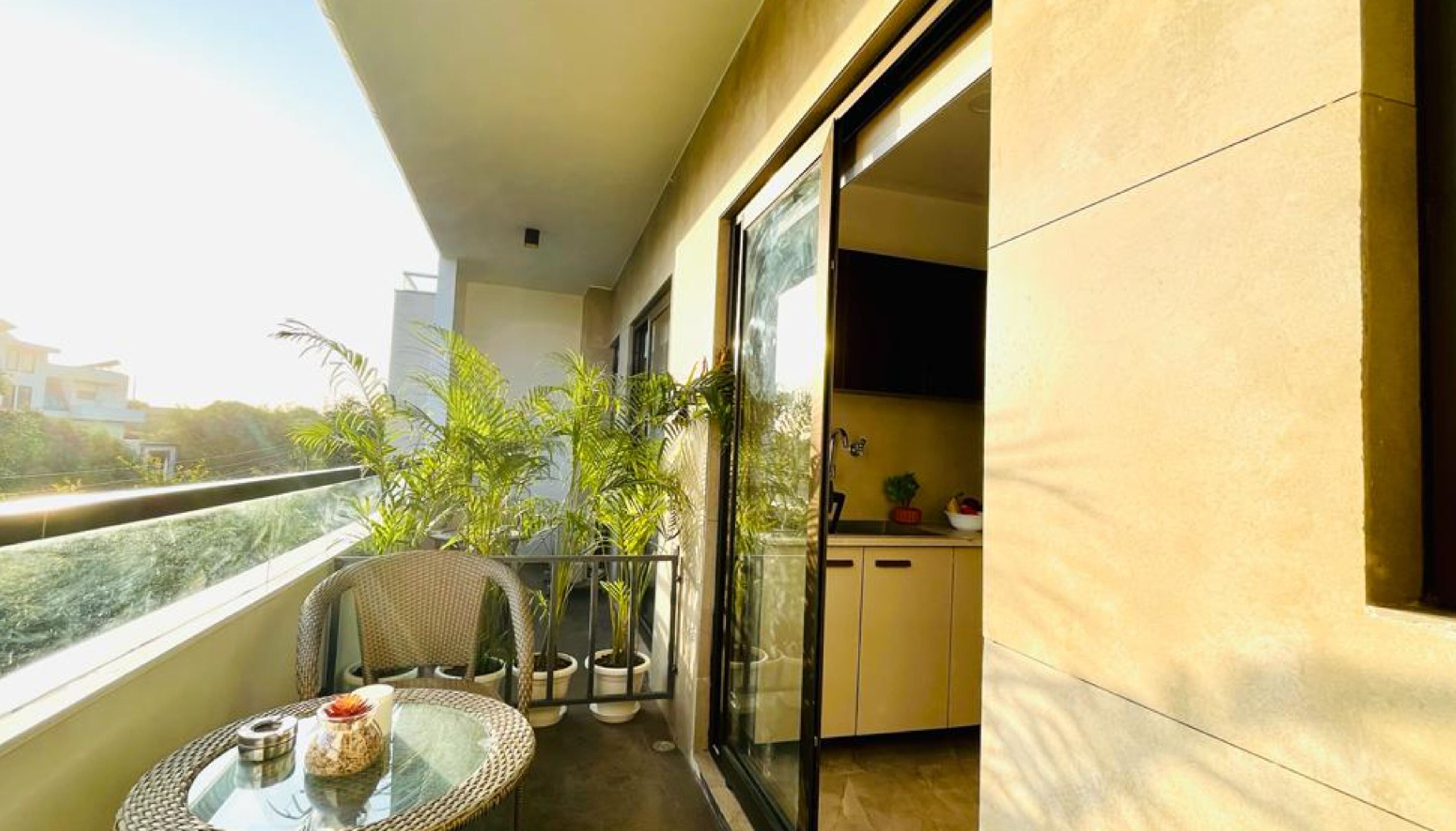 Un balcón con puerta de vidrio que da a una cocina, plantas en macetas y una silla de mimbre.