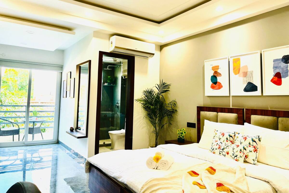 Une chambre d’hôtel moderne dotée d’un grand lit, d’un ventilateur de plafond, d’une salle de bain avec une porte en verre et d’œuvres d’art accrochées aux murs.
