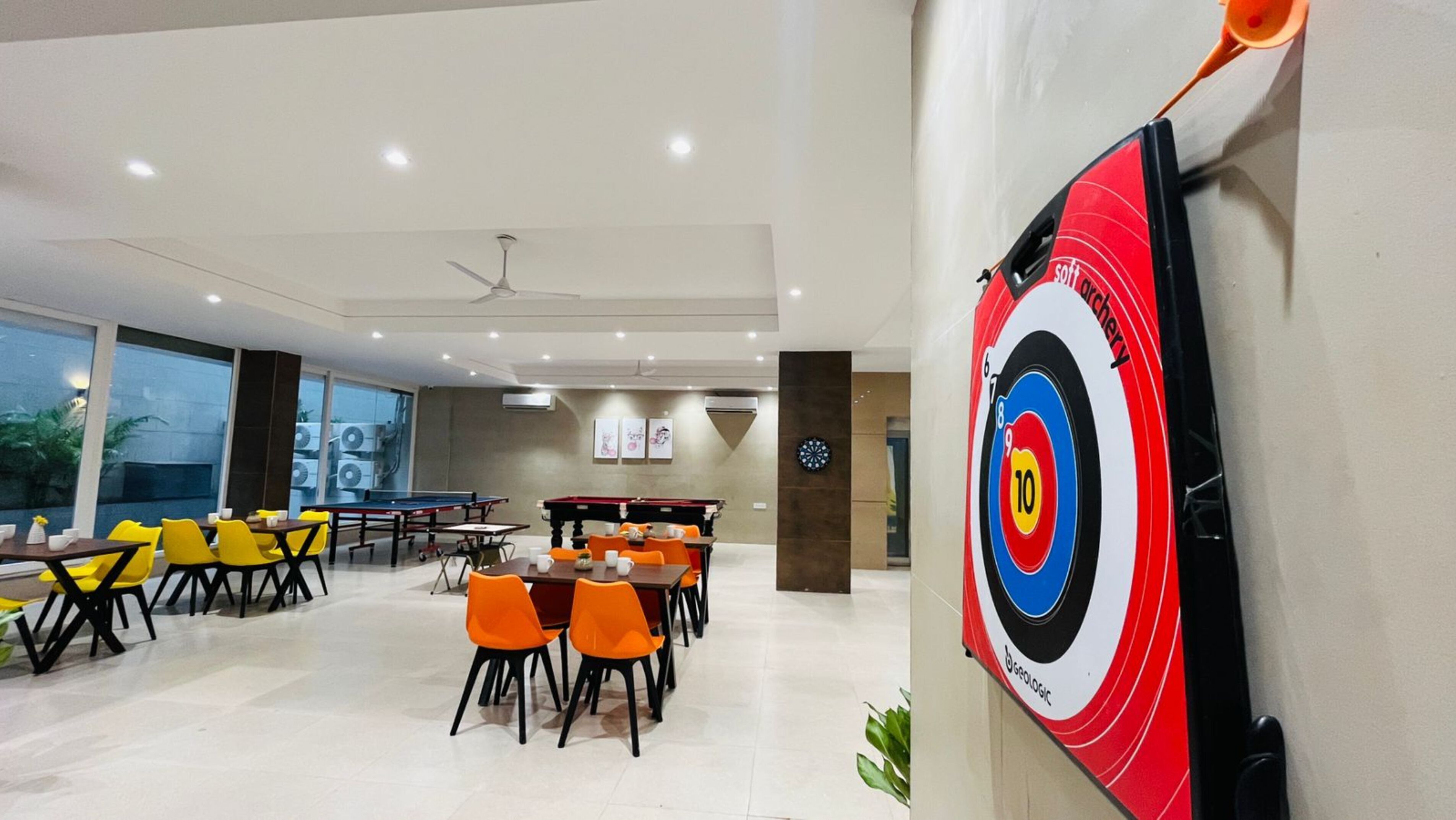 A modern indoor space with ping pong tables, orange chairs, and a dartboard on the wall.