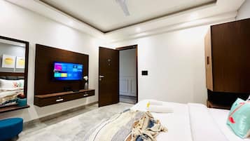 A modern hotel room with a large bed, a flat-screen TV mounted on the wall, a wooden wardrobe, and a small side table with a vase.