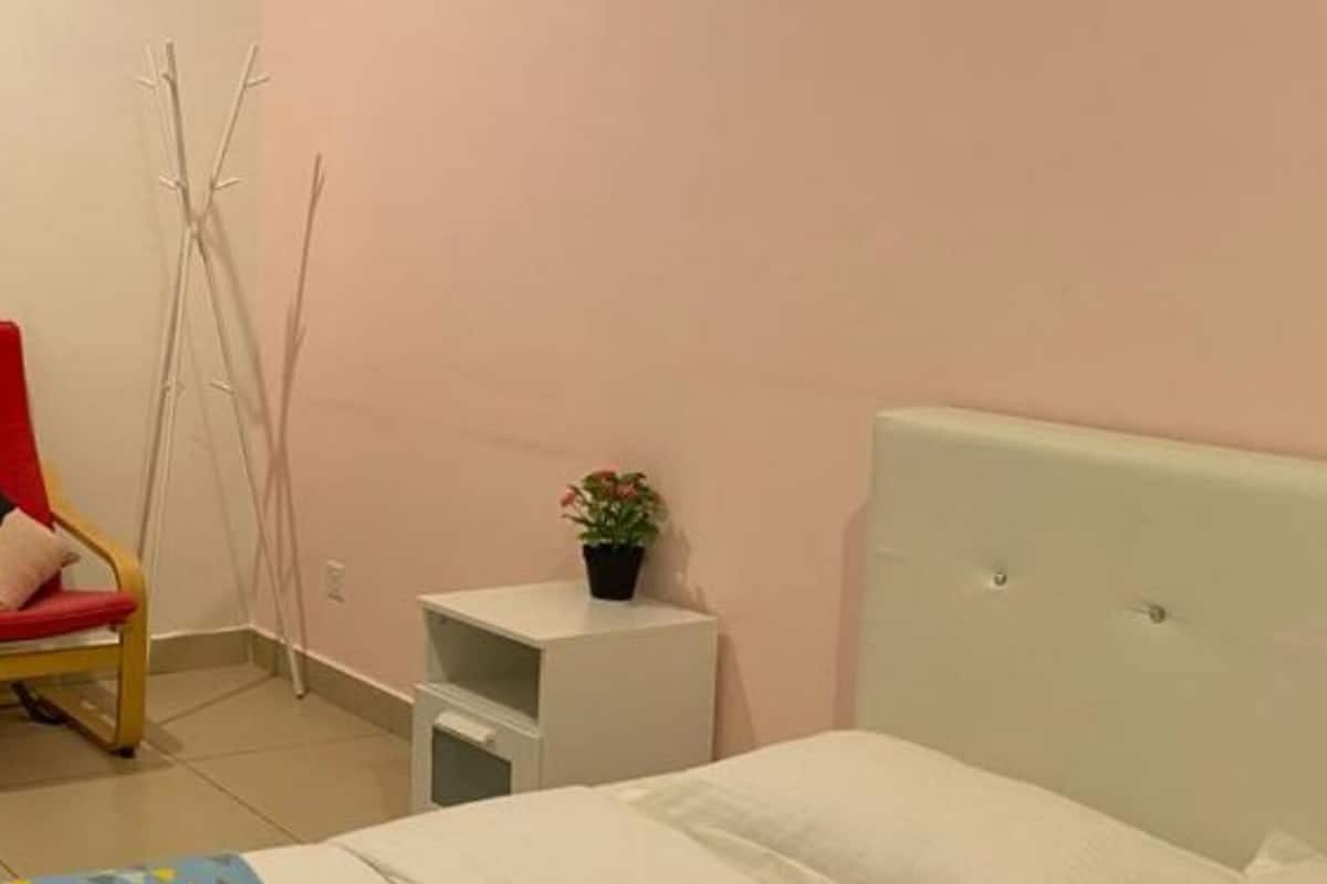 A bedroom with a bed, a nightstand, a chair, and a potted plant.
