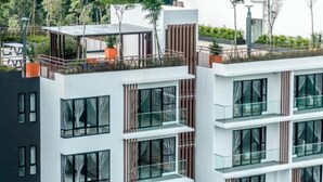 Un edificio de varios pisos con balcones, ventanas grandes y un jardín en la azotea.