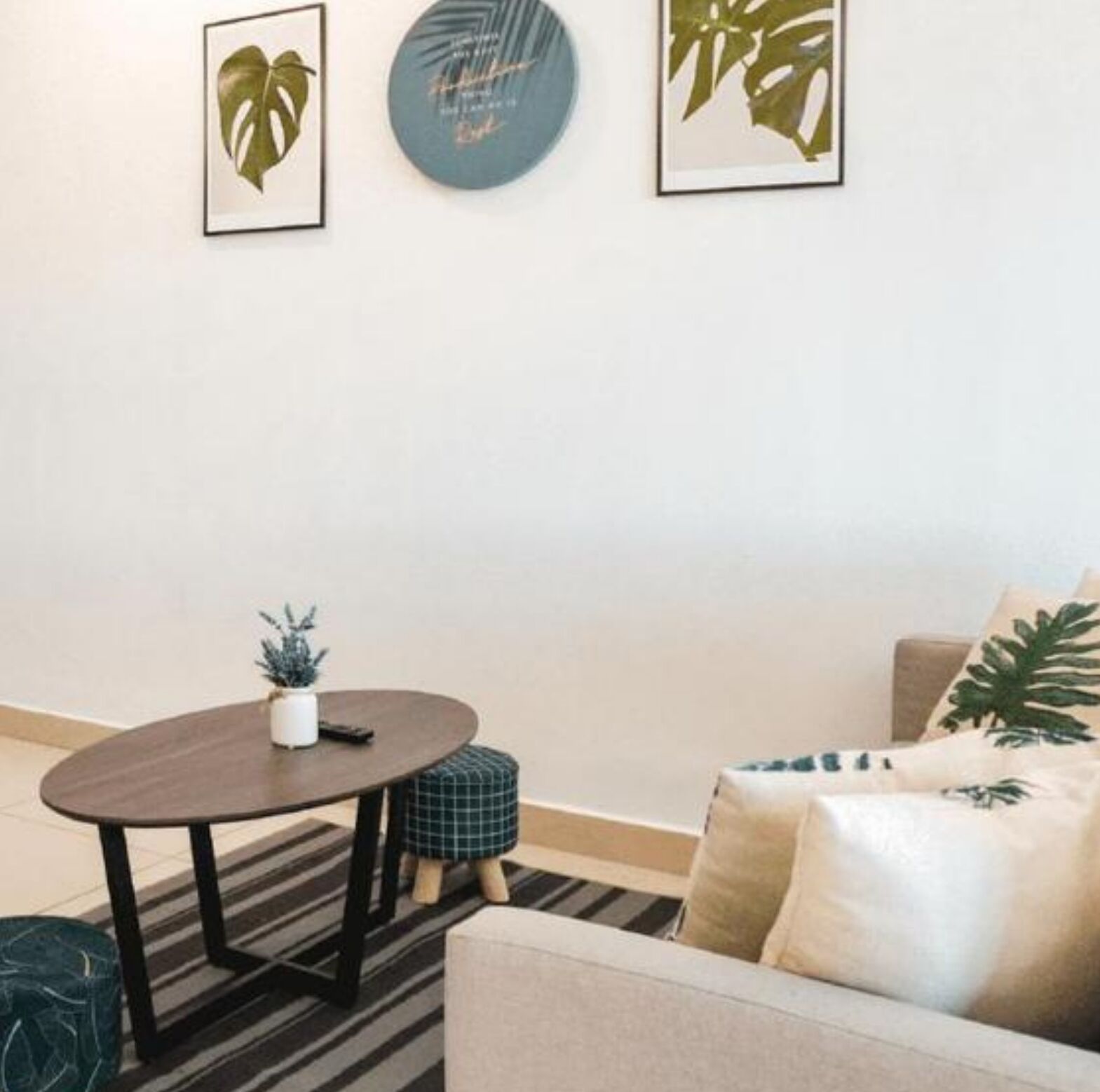 A living room with a round table, a sofa, and a coffee table. There are framed pictures on the wall and a potted plant on the table.