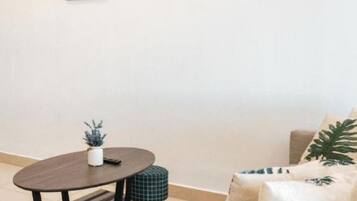 A living room with a round table, a sofa, and a coffee table. There are framed pictures on the wall and a potted plant on the table.