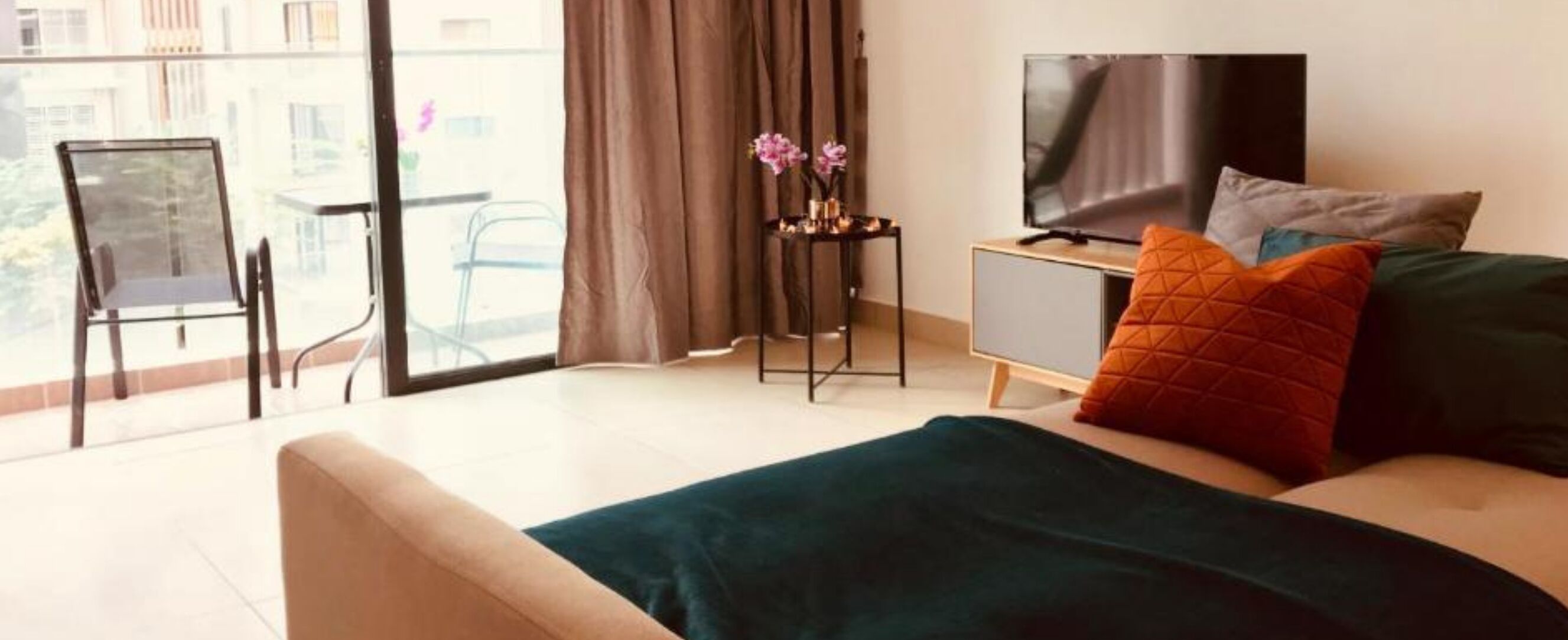 Une chambre d’hôtel moderne avec un grand lit, une télévision, une petite table agrémentée de fleurs et un balcon avec une chaise.