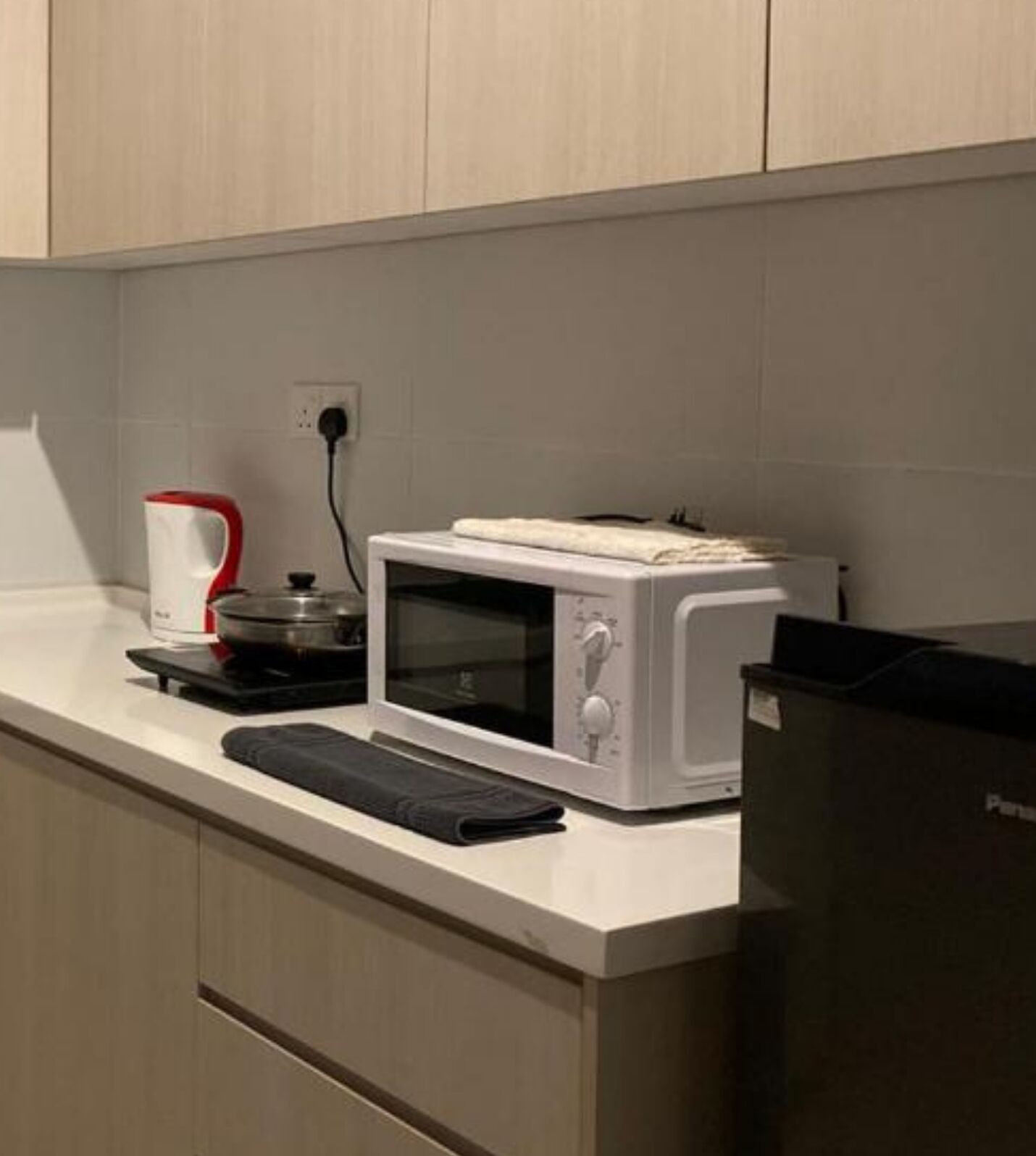 A kitchen with a microwave, a kettle, and a black appliance on the counter.